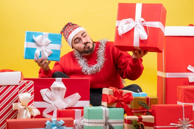 Photo gratuite vue de face jeune homme assis autour de cadeaux de noël sur fond jaune