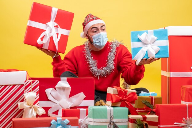 Vue de face jeune homme assis autour de cadeaux de Noël sur fond jaune