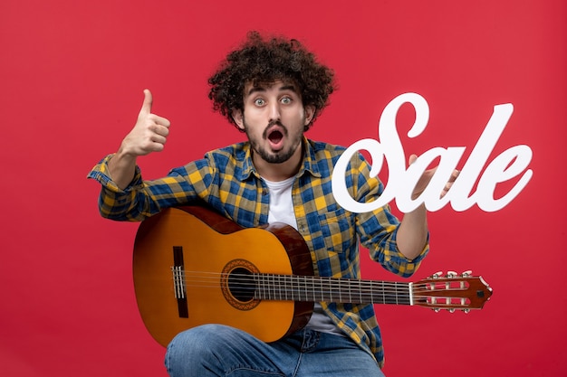 Photo gratuite vue de face jeune homme assis avec guitare sur mur rouge concert de musique applaudissements couleur vente en direct