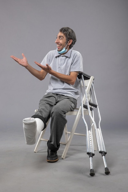 Photo gratuite vue de face jeune homme assis avec un pied cassé bandé sur un bureau gris douleur torsion jambe accident pied masculin