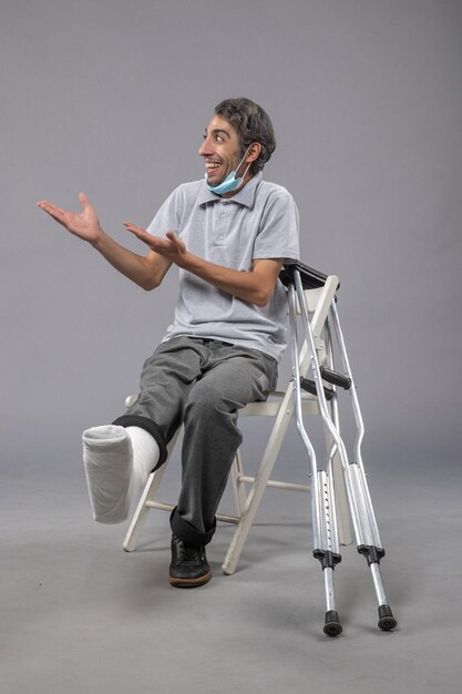 Vue de face jeune homme assis avec un pied cassé bandé sur un bureau gris douleur torsion jambe accident pied masculin