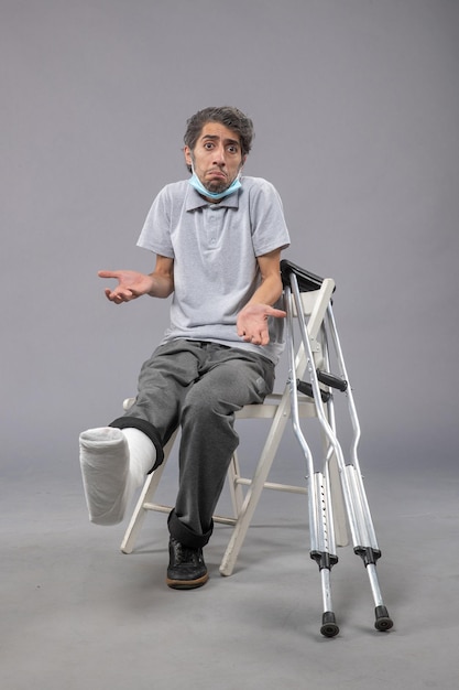 Vue de face jeune homme assis avec un pied cassé bandé sur le mur gris douleur torsion jambe accident pied masculin