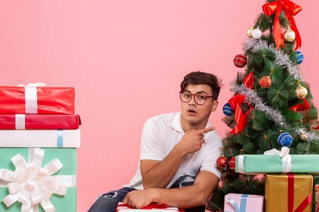 Vue de face jeune homme autour de cadeaux et arbre de Noël sur le fond rose