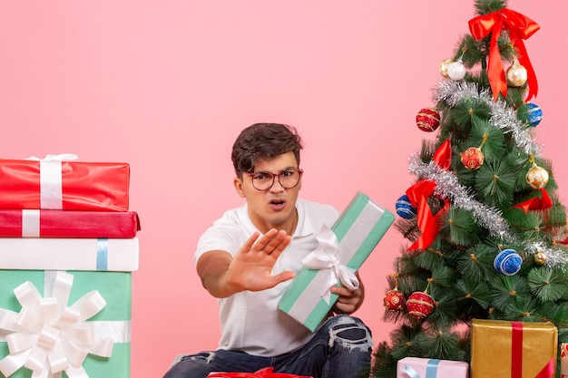 Vue de face jeune homme autour de cadeaux et arbre de Noël sur le fond rose