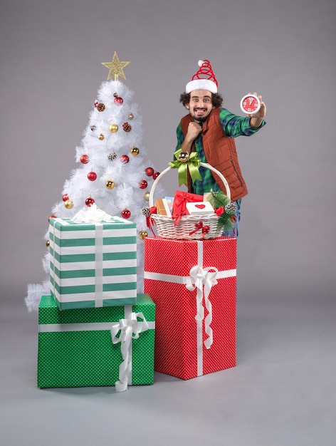 Vue de face jeune homme autour de cadeaux de vacances sur le gris