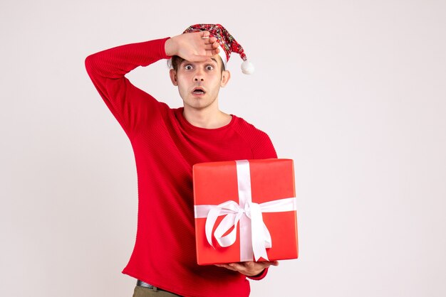 Vue de face jeune homme aux yeux écarquillés avec bonnet de Noel debout sur blanc