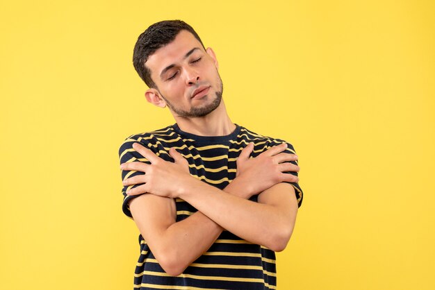 Vue de face jeune homme aux yeux fermés croisant les mains sur fond isolé jaune