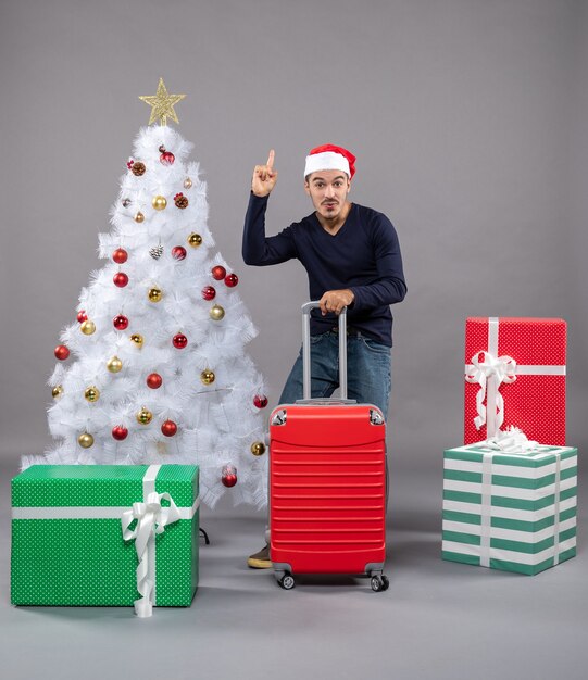 Vue de face jeune homme avec bonnet de noel apparaissant sur gris isolé