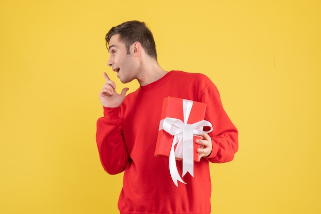 Vue de face jeune homme avec cadeau de Noël debout sur fond jaune