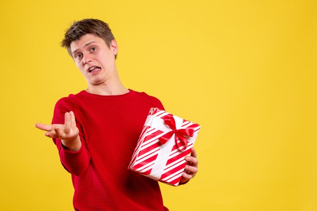 Vue de face jeune homme avec cadeau de Noël sur fond jaune