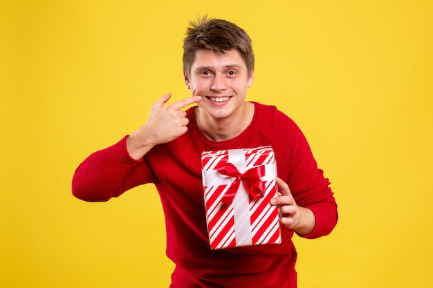 Vue de face jeune homme avec cadeau de Noël sur fond jaune