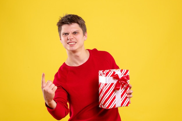 Vue de face jeune homme avec cadeau de Noël sur fond jaune