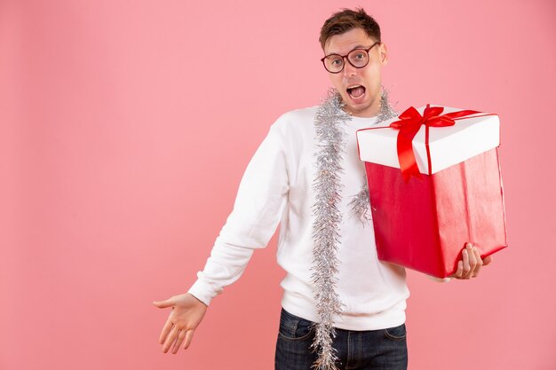 Vue de face jeune homme avec cadeau de Noël sur fond rose