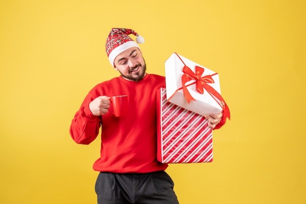 Vue de face jeune homme avec cadeau de Noël et tasse de thé sur fond jaune