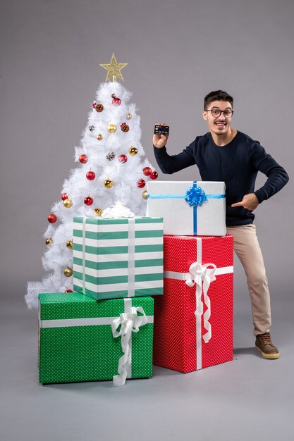 Vue de face jeune homme avec cadeaux et carte bancaire sur le gris