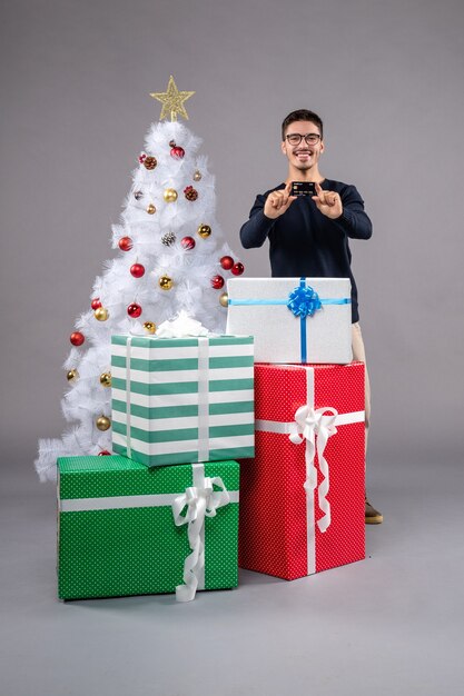 Vue de face jeune homme avec cadeaux et carte bancaire sur le gris