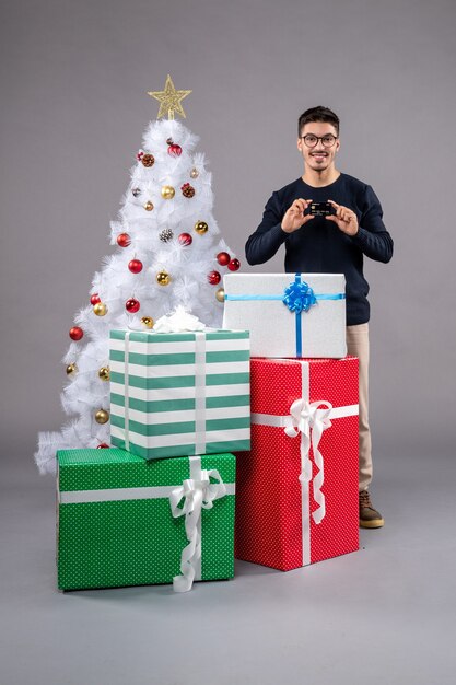 Vue de face jeune homme avec cadeaux et carte bancaire sur le gris