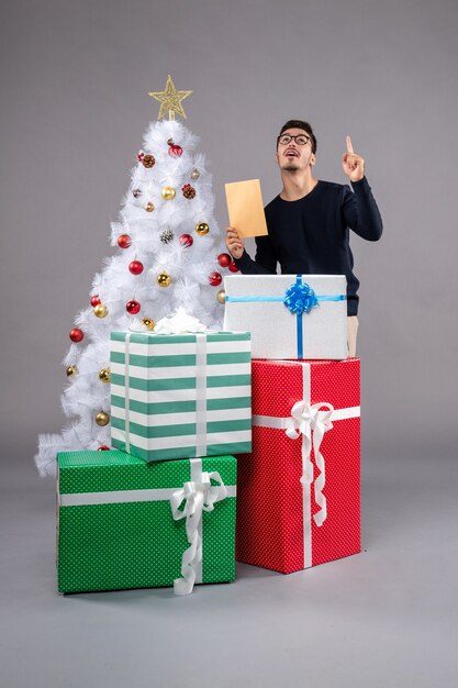 Vue de face jeune homme avec des cadeaux et enveloppe sur un bureau lumineux vacances nouvel an noël