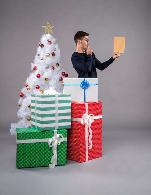 Photo gratuite vue de face jeune homme avec des cadeaux et enveloppe sur le gris