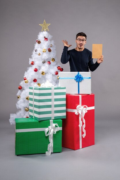 Vue de face jeune homme avec des cadeaux et enveloppe sur la lumière