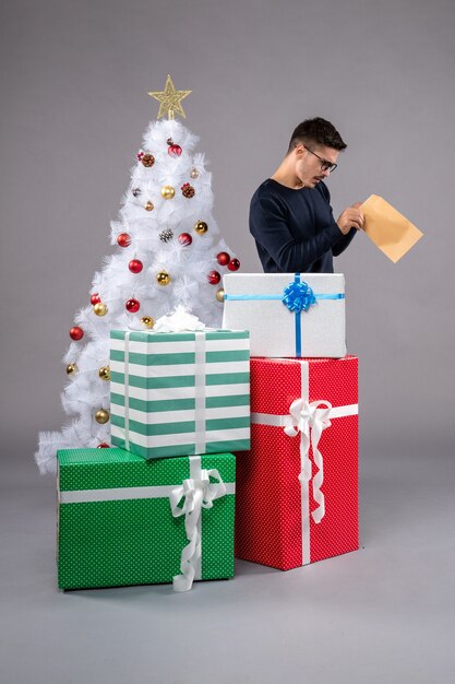 Vue de face jeune homme avec des cadeaux et enveloppe sur la lumière