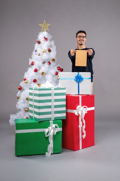 Vue de face jeune homme avec des cadeaux et enveloppe sur sol clair vacances nouvel an noël