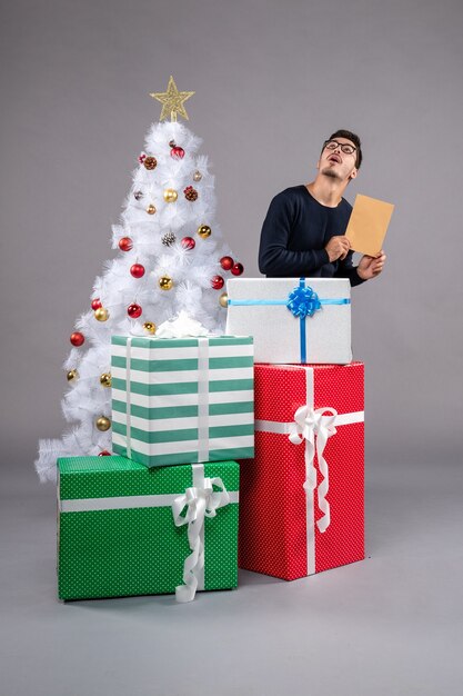 Vue de face jeune homme avec des cadeaux et enveloppe sur sol clair vacances nouvel an noël