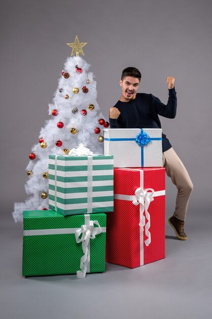 Vue de face jeune homme avec des cadeaux de noël sur un bureau gris cadeau de noël du nouvel an