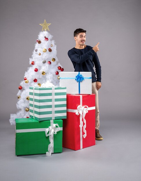 Vue de face jeune homme avec des cadeaux de noël sur un bureau lumineux vacances de noël nouvel an