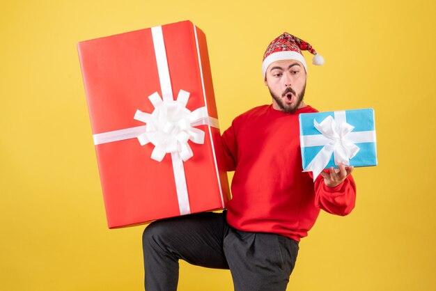 Vue de face jeune homme avec des cadeaux de Noël sur fond jaune