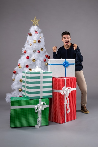 Vue de face jeune homme avec des cadeaux de Noël sur le gris