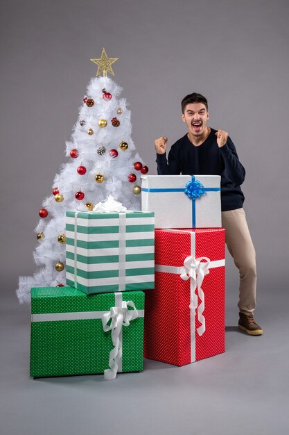 Vue de face jeune homme avec des cadeaux de Noël sur le gris