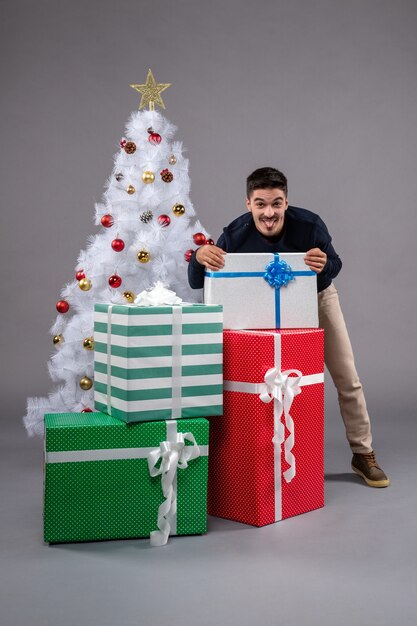 Vue de face jeune homme avec des cadeaux de Noël sur le gris