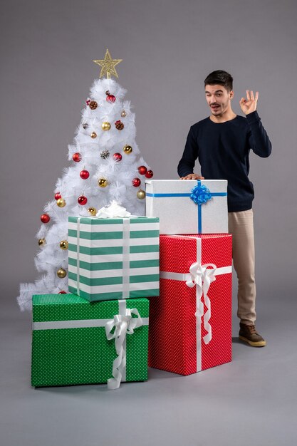 Vue de face jeune homme avec des cadeaux de noël sur sol gris cadeau de nouvel an noël