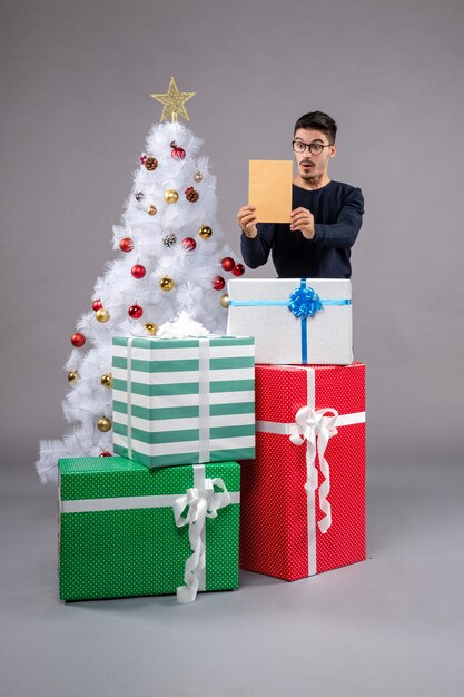 Vue de face jeune homme avec des cadeaux de vacances sur un bureau gris cadeau nouvel an humain de Noël