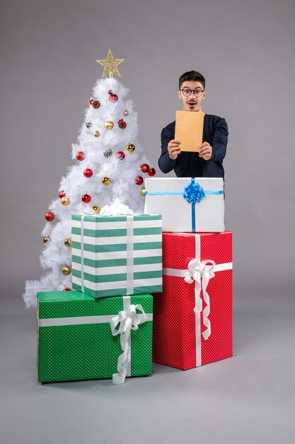 Vue de face jeune homme avec des cadeaux de vacances sur gris