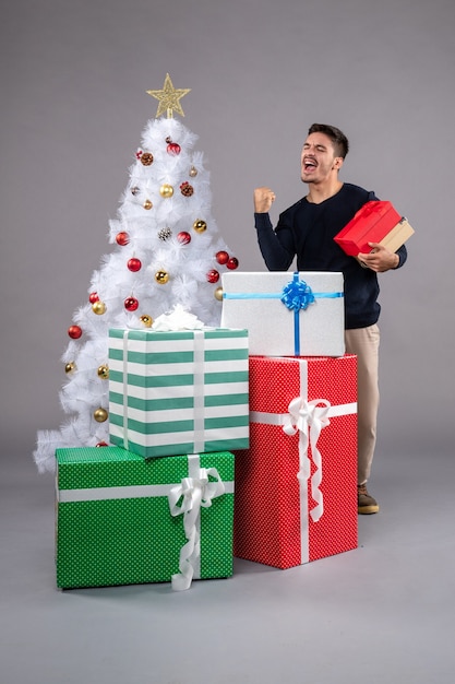 Vue de face jeune homme avec des cadeaux de vacances sur gris