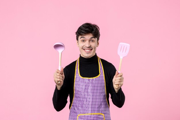 Vue De Face Jeune Homme En Cape Avec Cuillères Sur Fond Rose Nourriture Couleur Cuisson Pâte Horizontale Cuisine Profession Travail