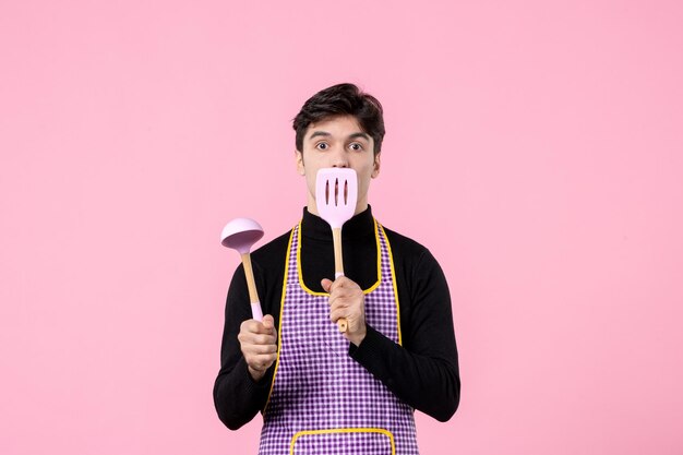Vue de face jeune homme en cape avec cuillères sur fond rose nourriture couleur cuisson uniforme travail horizontal cuisine profession
