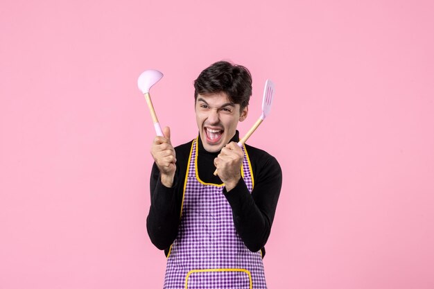 Vue de face jeune homme en cape tenant des cuillères sur fond rose couleur repas pâte horizontale cuisine profession travail nourriture uniforme