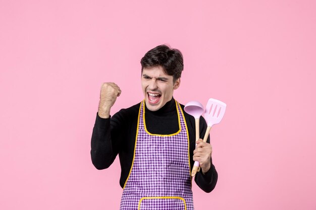 Vue de face jeune homme en cape tenant des cuillères sur fond rose profession nourriture cuisine repas couleur horizontale travail de pâte uniforme