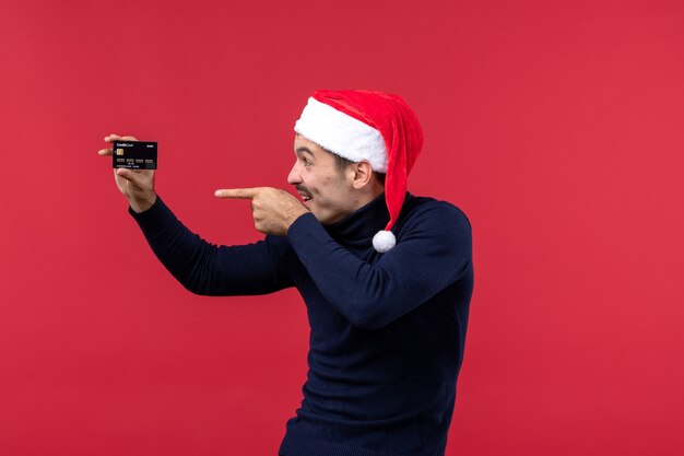 Vue de face jeune homme avec carte bancaire noire sur fond rouge