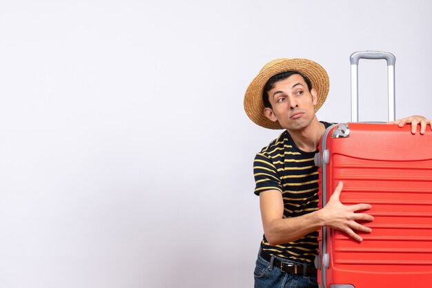 Vue de face jeune homme avec chapeau de paille tenant valise rouge