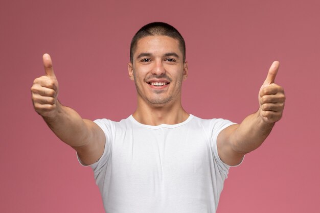 Vue de face jeune homme en chemise blanche montrant comme des signes souriant sur fond rose