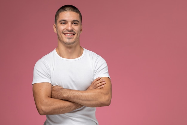 Vue de face jeune homme en chemise blanche regardant la caméra et souriant sur le fond rose