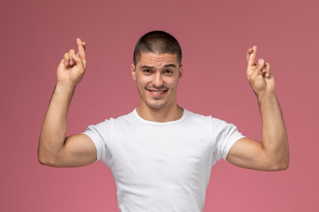 Vue de face jeune homme en chemise blanche souriant avec les doigts croisés sur fond rose