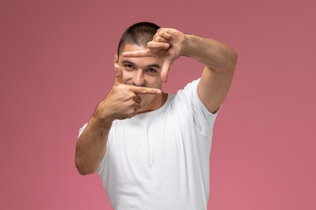 Vue de face jeune homme en chemise blanche souriant et prenant une photo sur fond rose