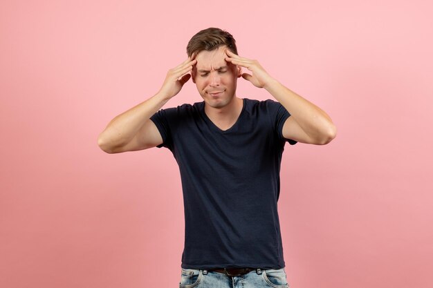 Vue de face jeune homme en chemise bleu foncé souffrant de maux de tête sur fond rose