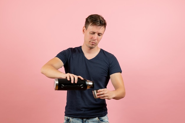 Vue de face jeune homme en chemise bleu foncé versant de l'eau du thermos sur fond rose