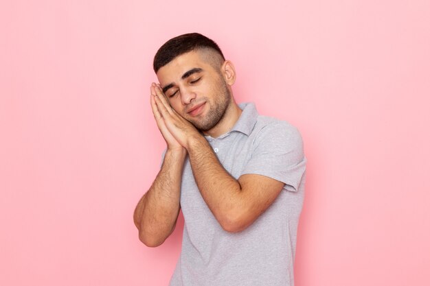 Vue de face jeune homme en chemise grise posant avec expression endormie sur rose